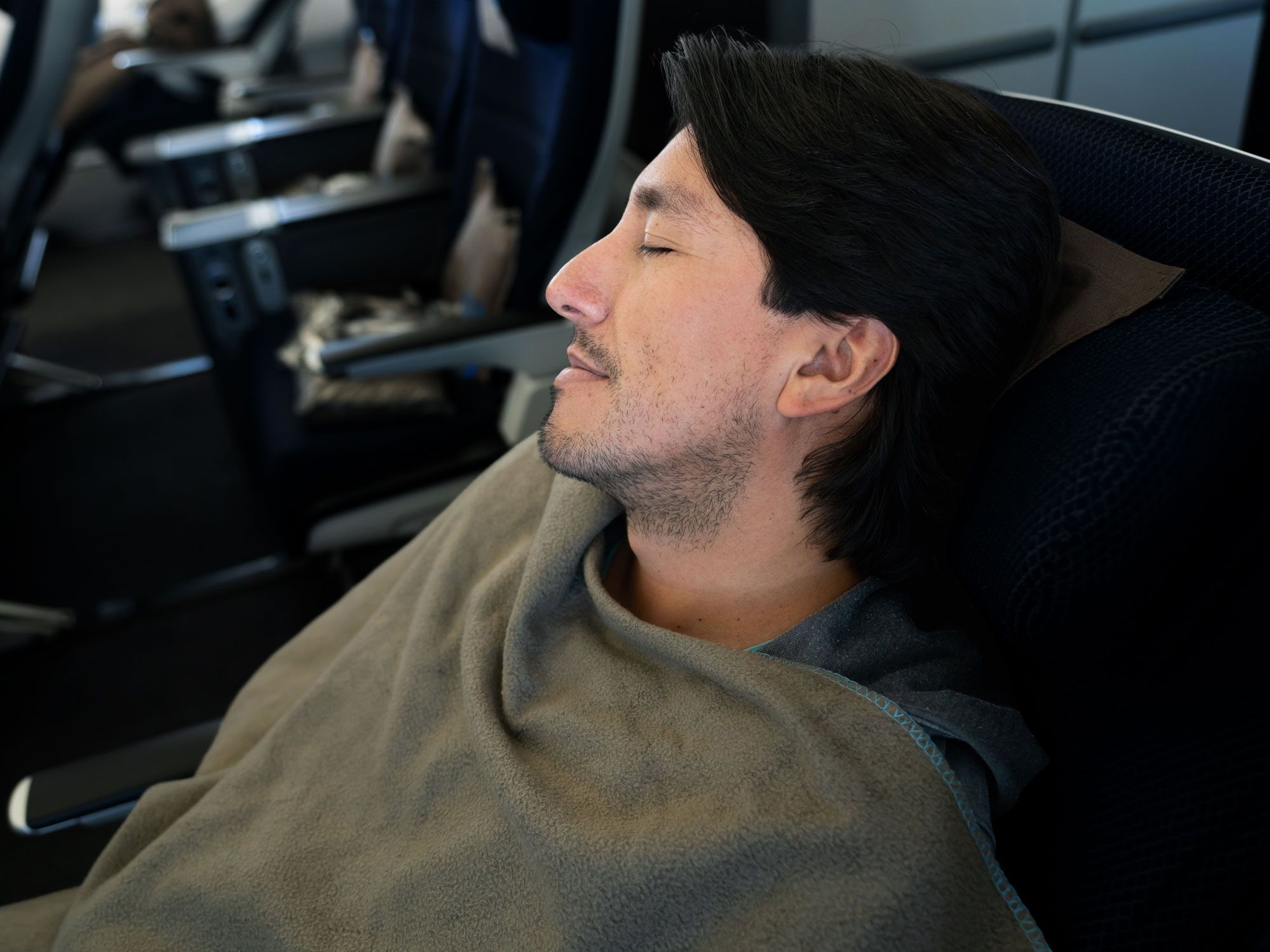 Traveler resting in plane seat with blanket