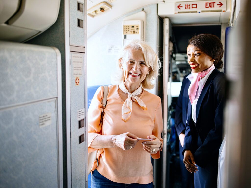 A flight attendant greets a passenger as she boards a plane