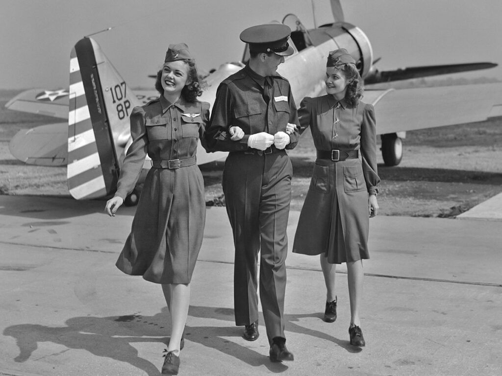 A male flight attendant walks with two female flight attendants in the 1940s