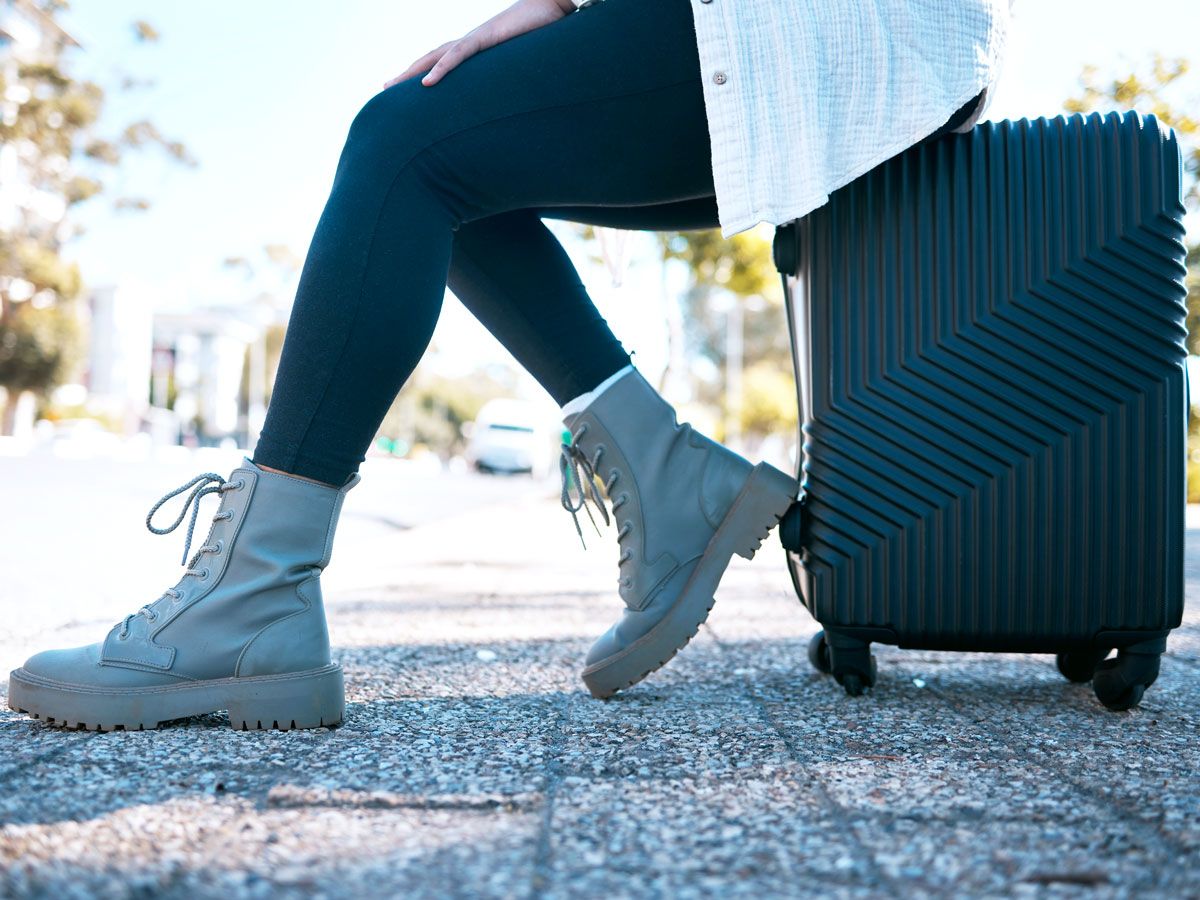 Traveler in lace-up boots sitting on suitcase