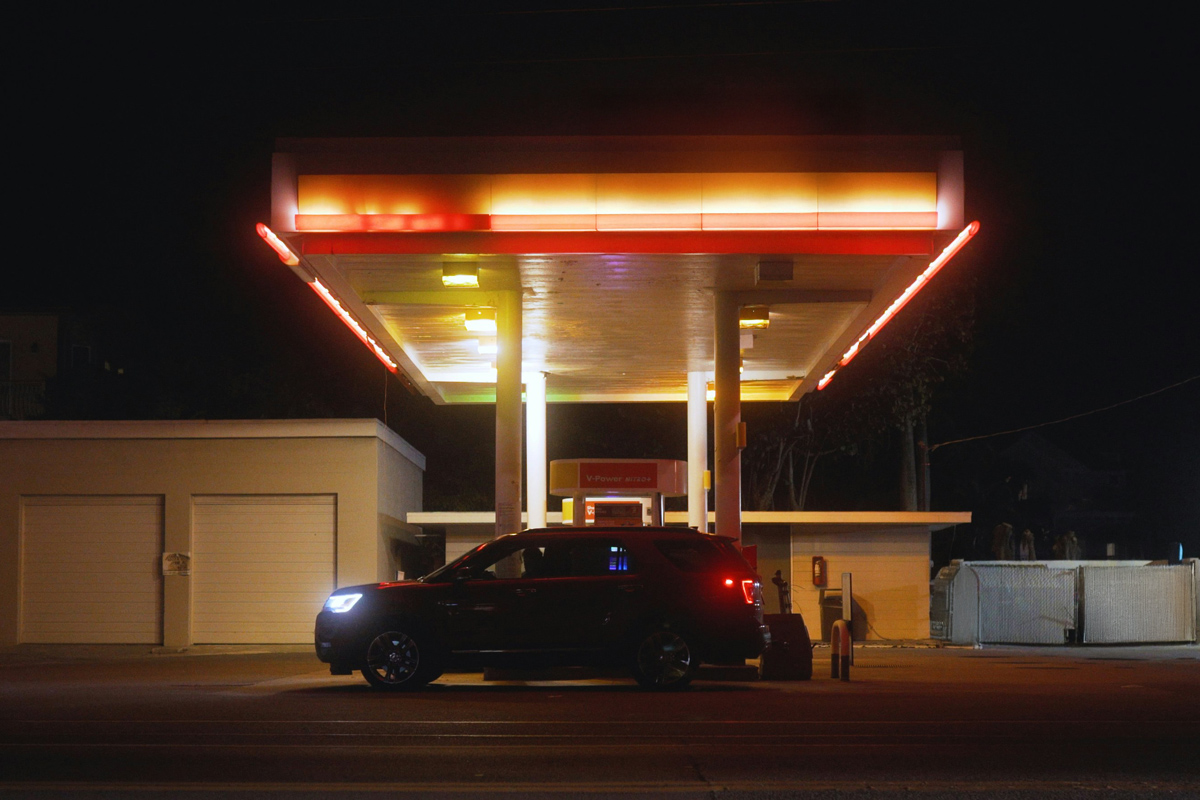 A car at a gas station at night lit up by neon lights