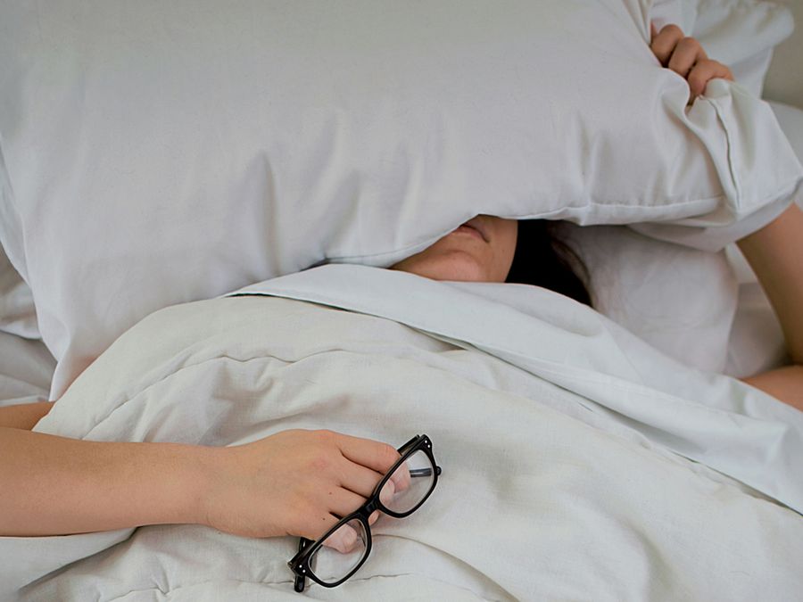 Person in bed holding pillow over their ears