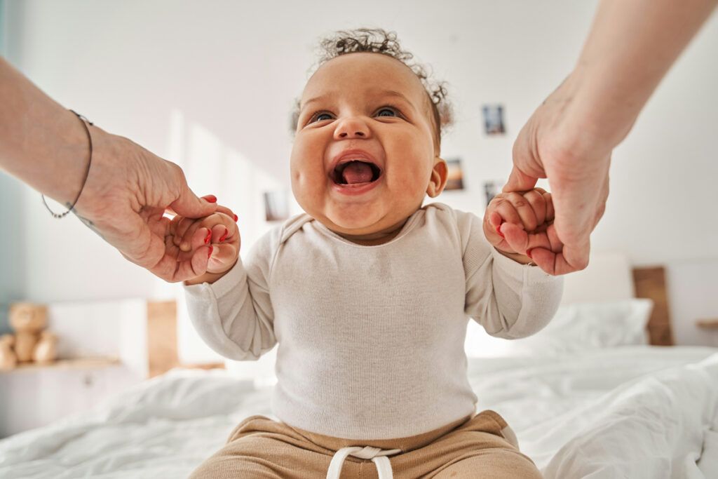 A laughing baby holding hands with an adult