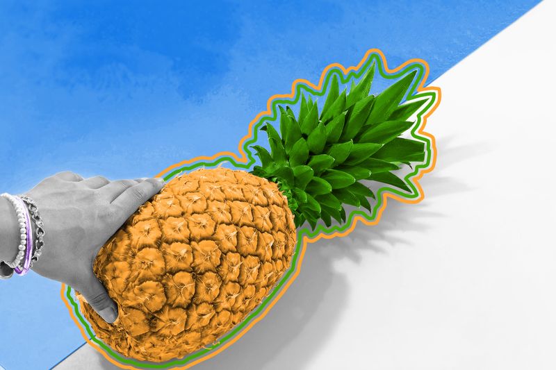 A hand holding a ripe pineapple next to pool side